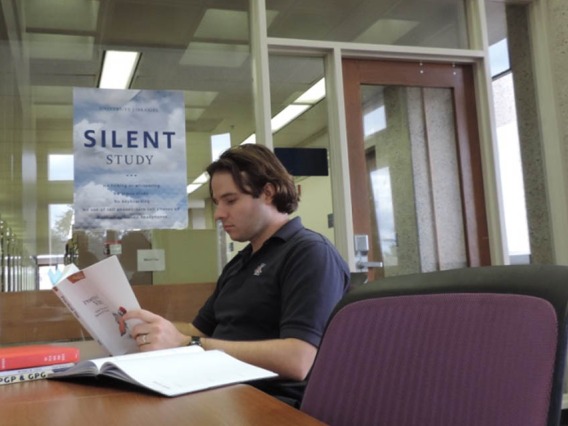 Man reading at a desk with sign for Silent Study Room in the background
