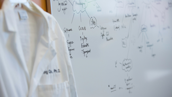 white coat hangs on hook next to a white board covered in notes